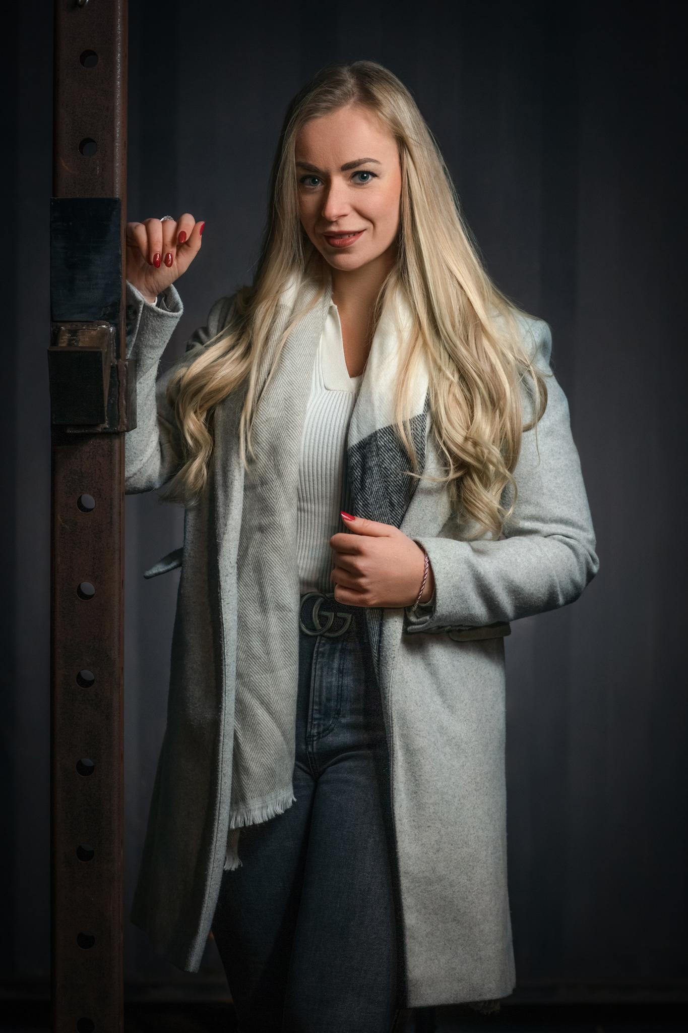 Stijlvol portret van een vrouw met lange blonde haren in een winterjas in een industriële setting